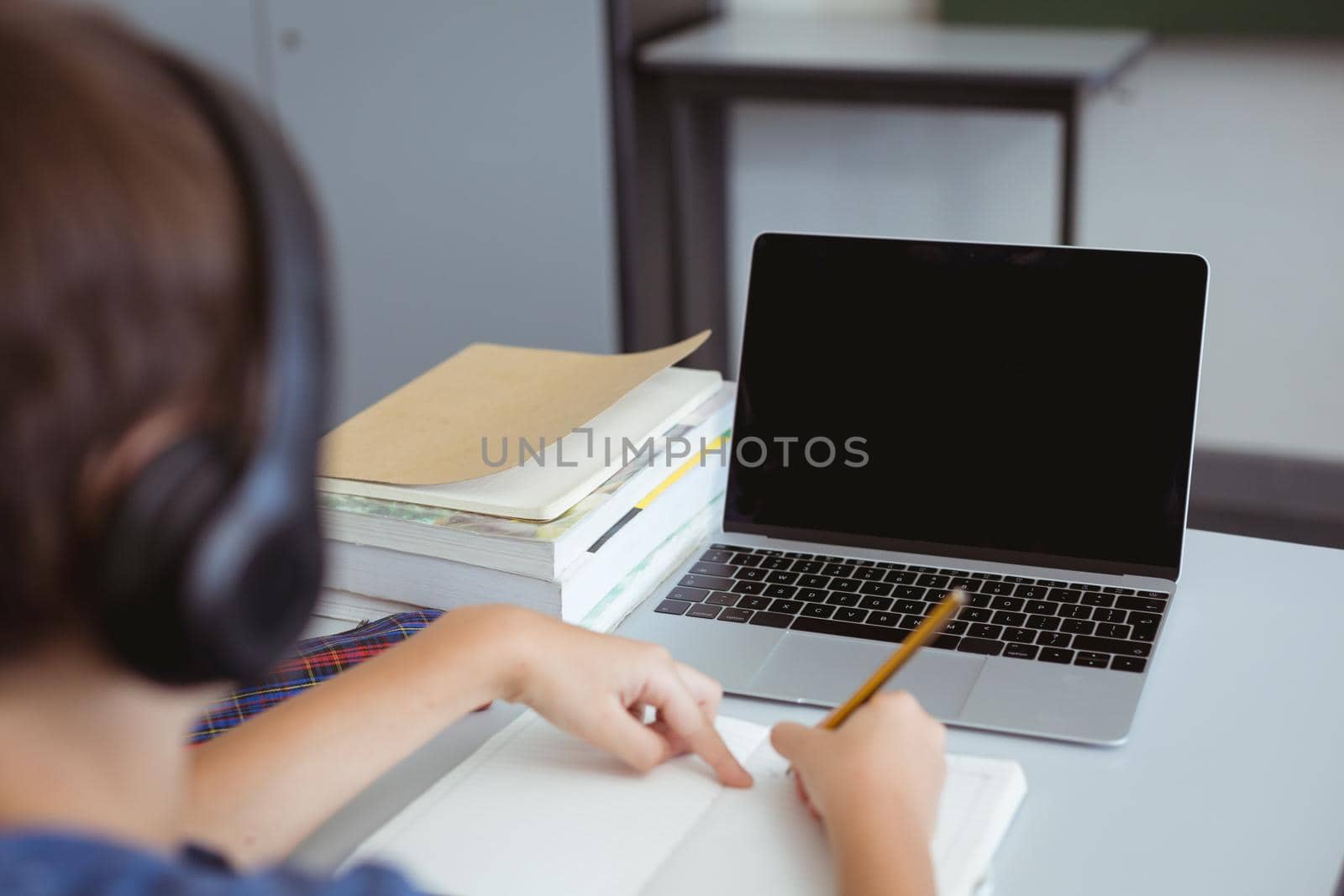 Caucasian schoolboy in classroom wearing headphones and using laptop, with copy space on screen. childhood, technology and education at elementary school.