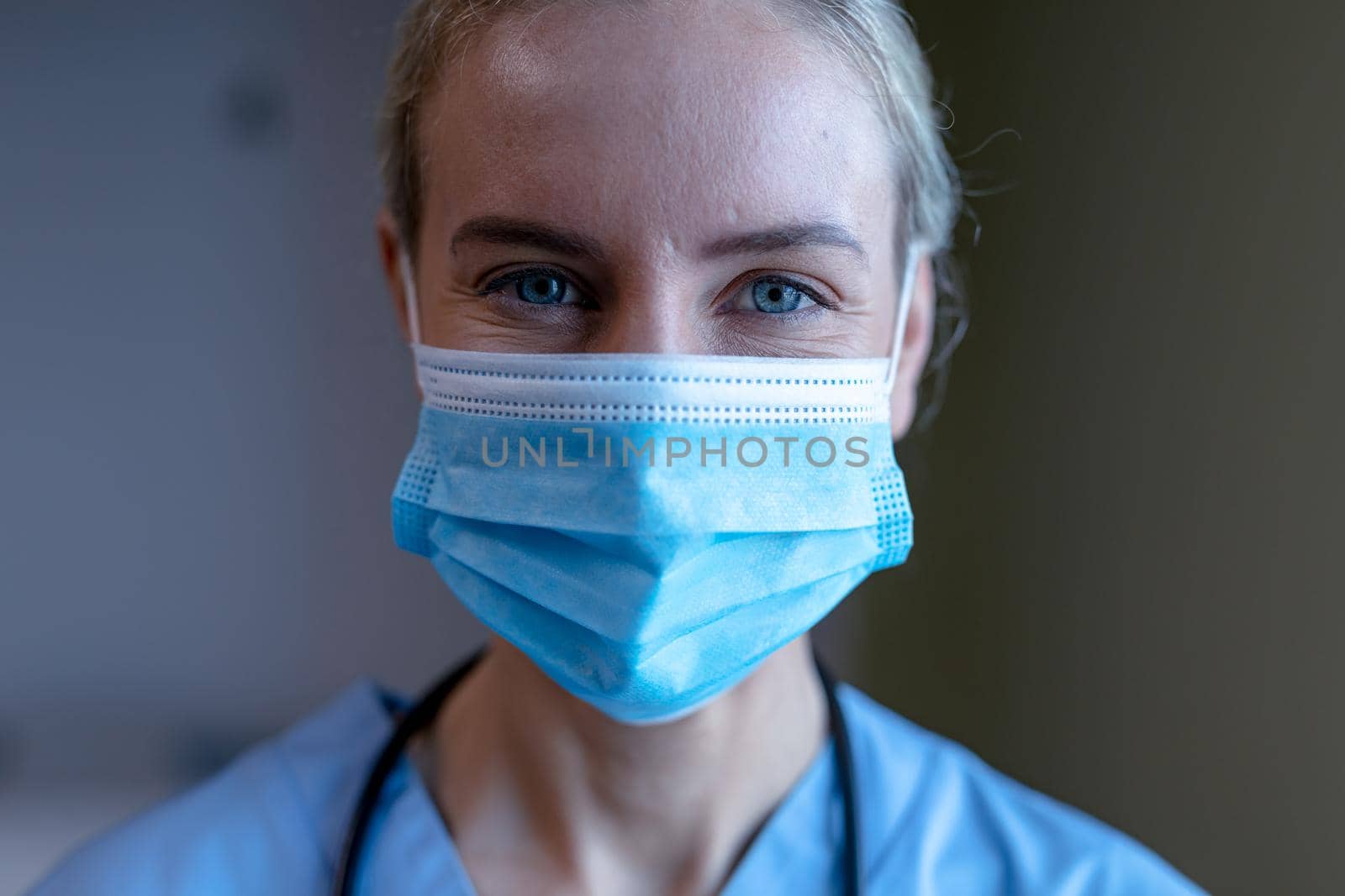Portrait of caucasian female doctor wearing face mask and scrubs looking to camera. medical professional at work and health services during coronavirus covid 19 pandemic.