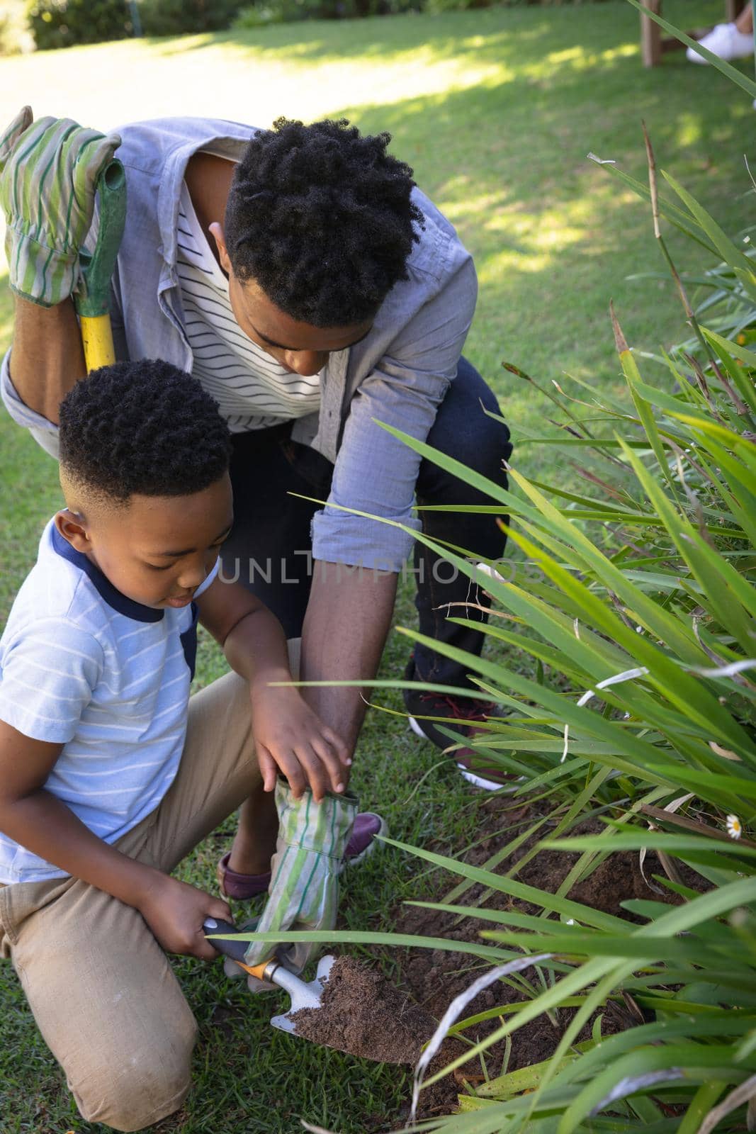 Happy african american father with son outdoors, gardening on sunny day. family enjoying quality free time together.
