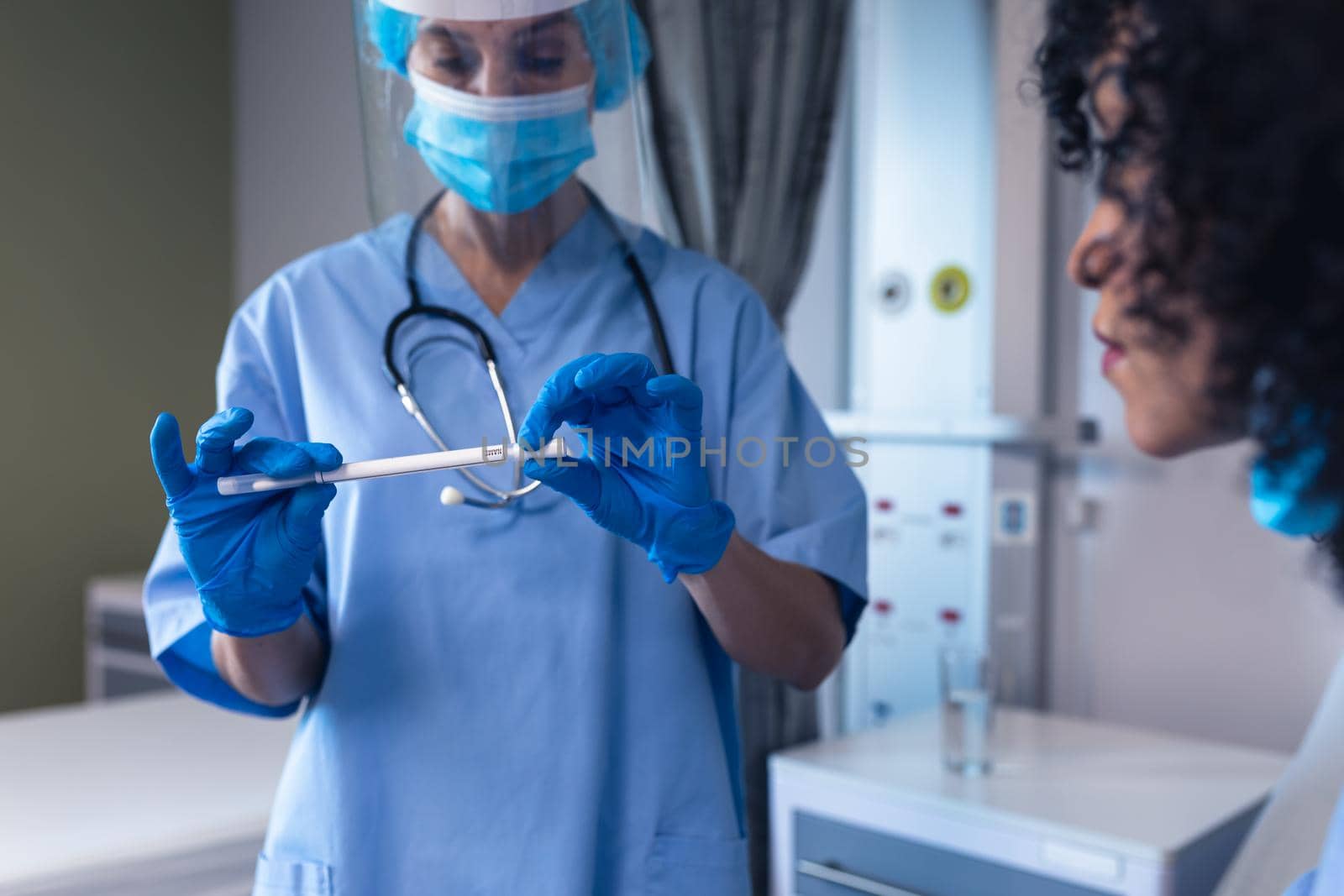 Caucasian female doctor in hospital wearing face mask holding swab test next to female patient. medical professional at work during coronavirus covid 19 pandemic.