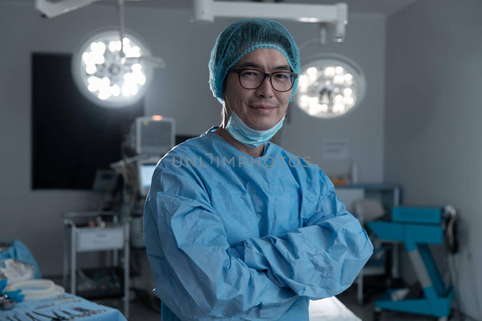 Portrait of asian male surgeon wearing lowered face mask, smiling in operating theatre. medicine, health and healthcare services during covid 19 coronavirus pandemic.