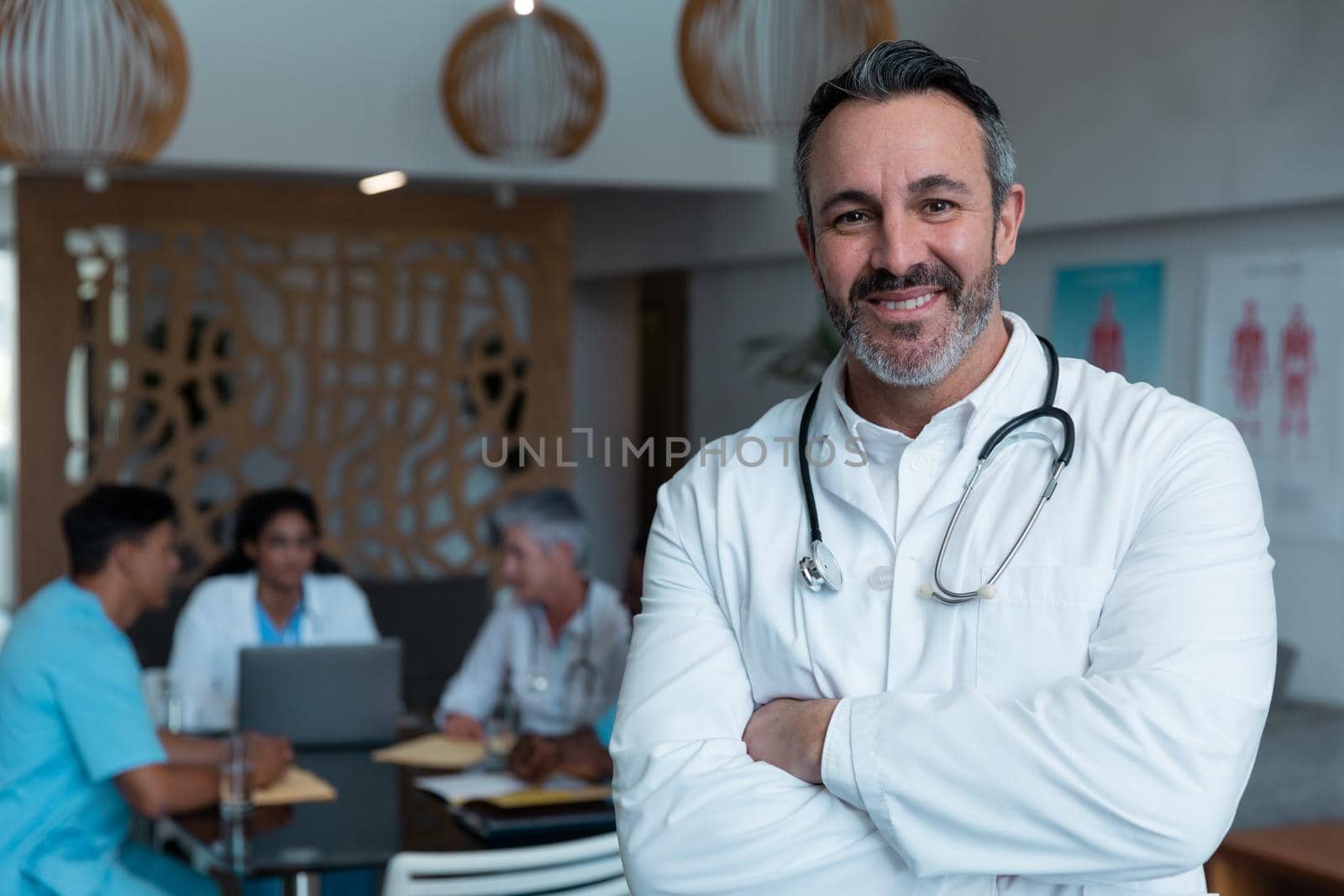 Portrait of smiling caucasian male doctor, with colleagues in discussion in the background by Wavebreakmedia