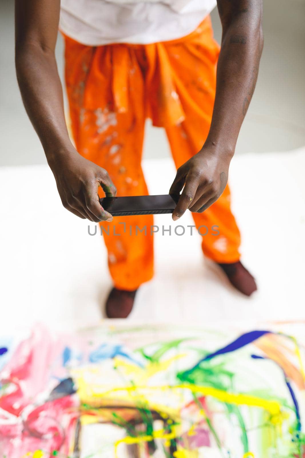 African american male painter at work taking picture of artwork with smartphone in art studio. creation and inspiration at an artists painting studio.