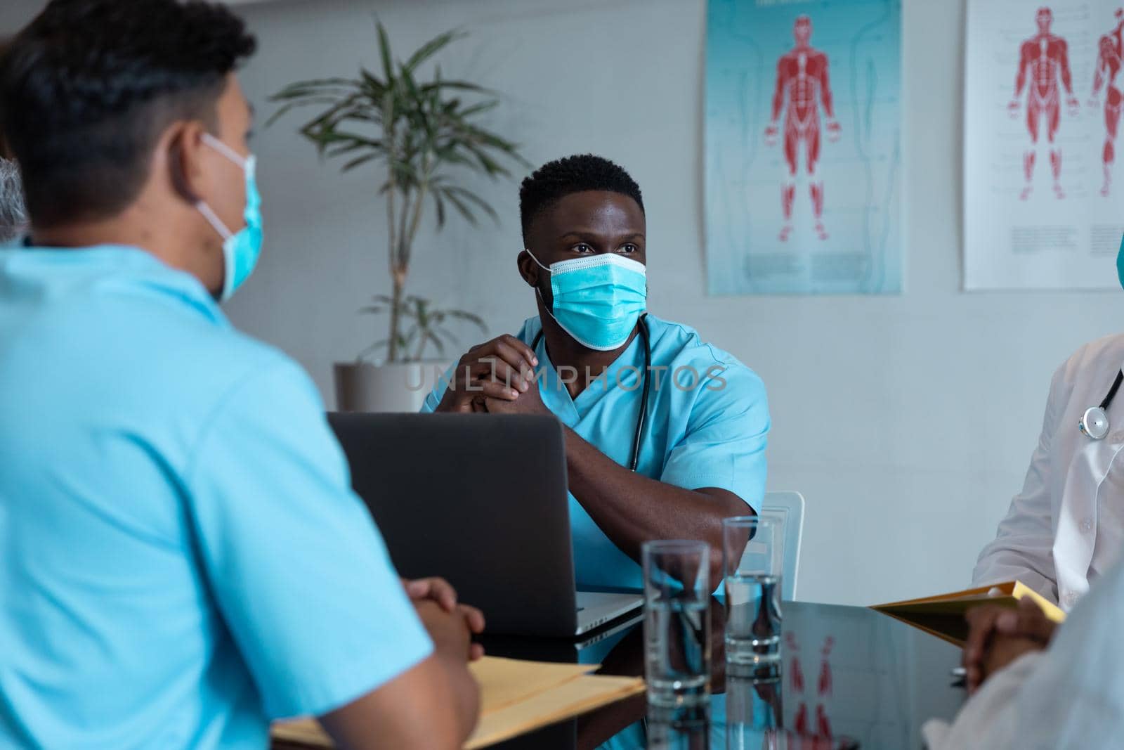 Diverse male and female doctors wearing face masks sitting in hospital having discussion. medicine, health and healthcare services during coronavirus covid 19 pandemic.