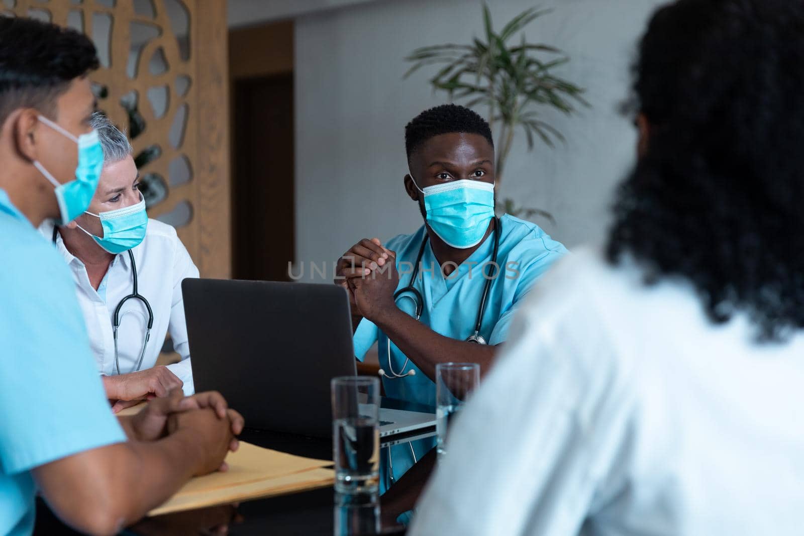 Diverse male and female doctors wearing face masks sitting in hospital having discussion. medicine, health and healthcare services during coronavirus covid 19 pandemic.