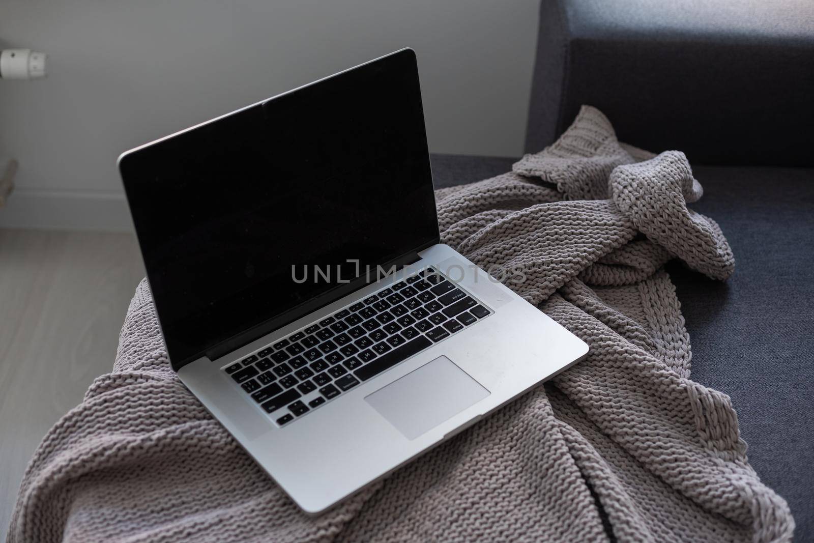 Laptop computer on grey sofa with blanket. Remote work at home office