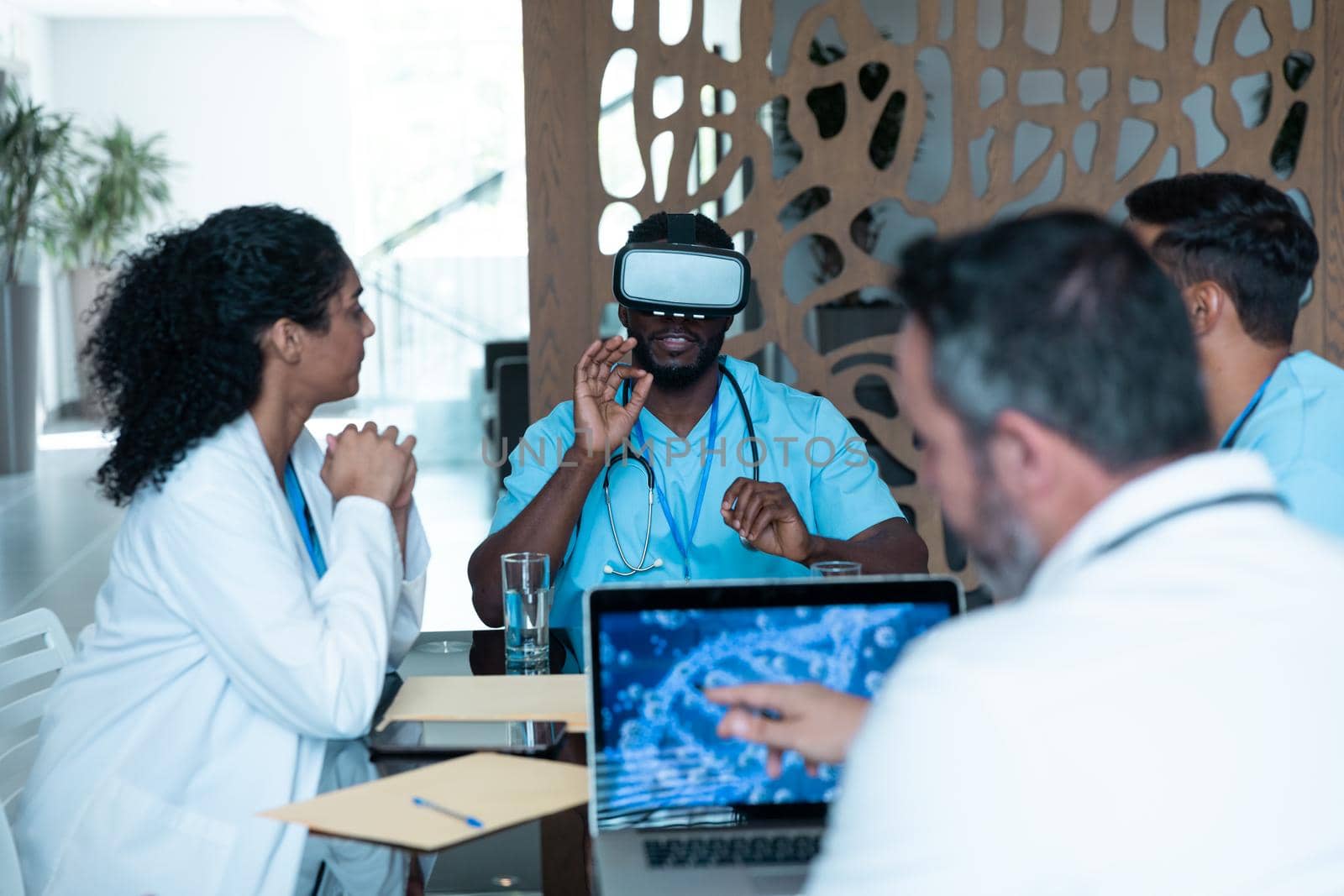 Diverse male and female doctors wearing face masks sitting at table and using vr glasses. medicine, health and healthcare services.