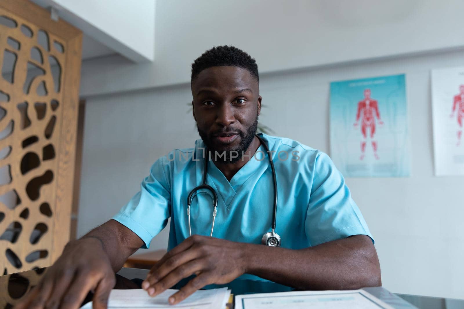 African american male doctor at desk talking and gesturing during video call consultation by Wavebreakmedia