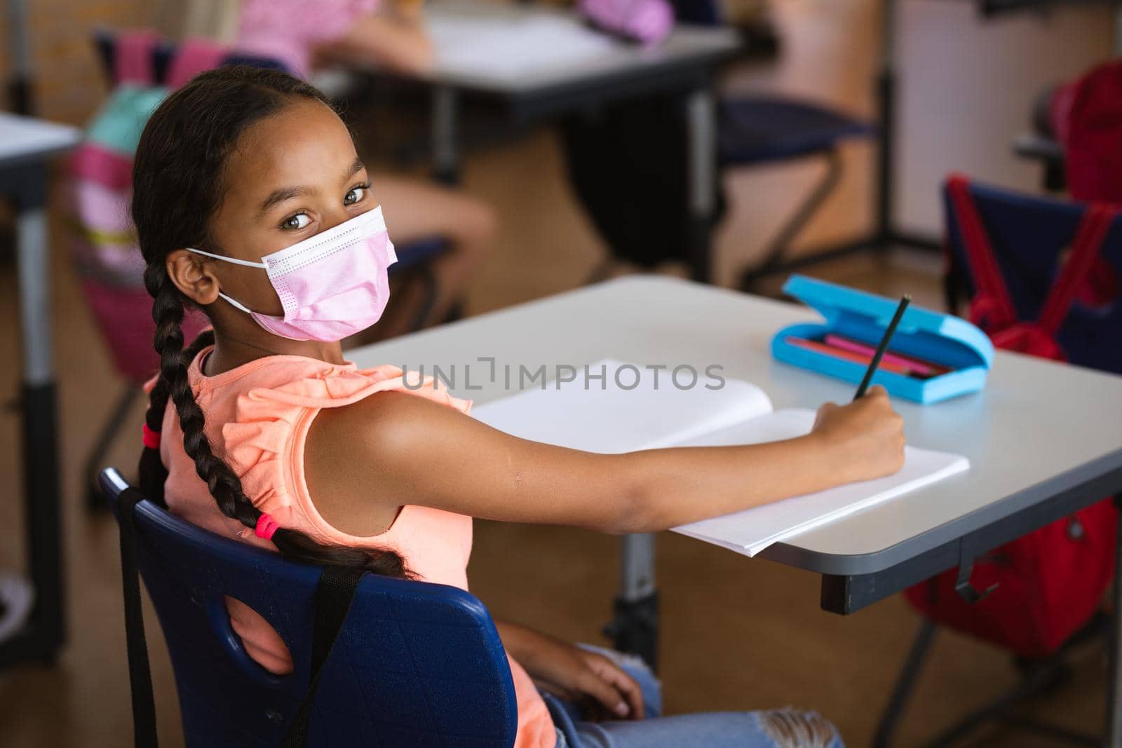 Portrait of african american girl wearing face mask sitting on her desk in the class at school. education back to school health safety during covid19 coronavirus pandemic