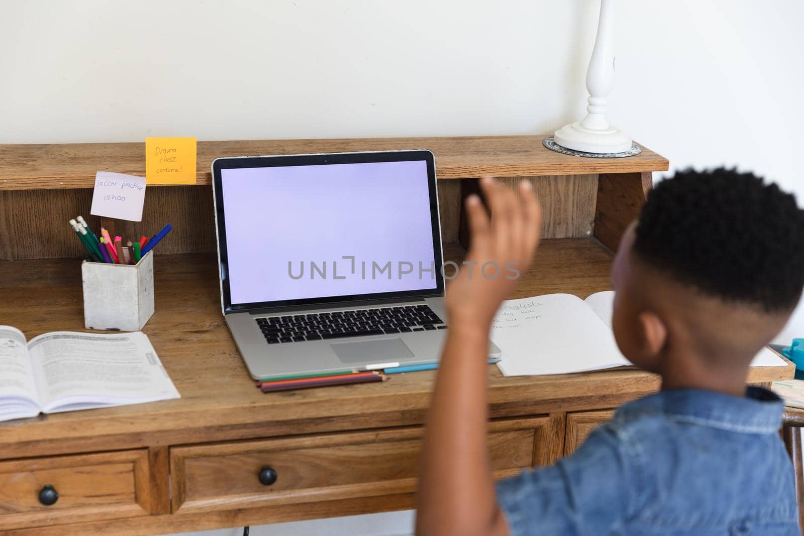 African american boy having video call lesson using laptop during class, raising hand at home. online education, learning at home.