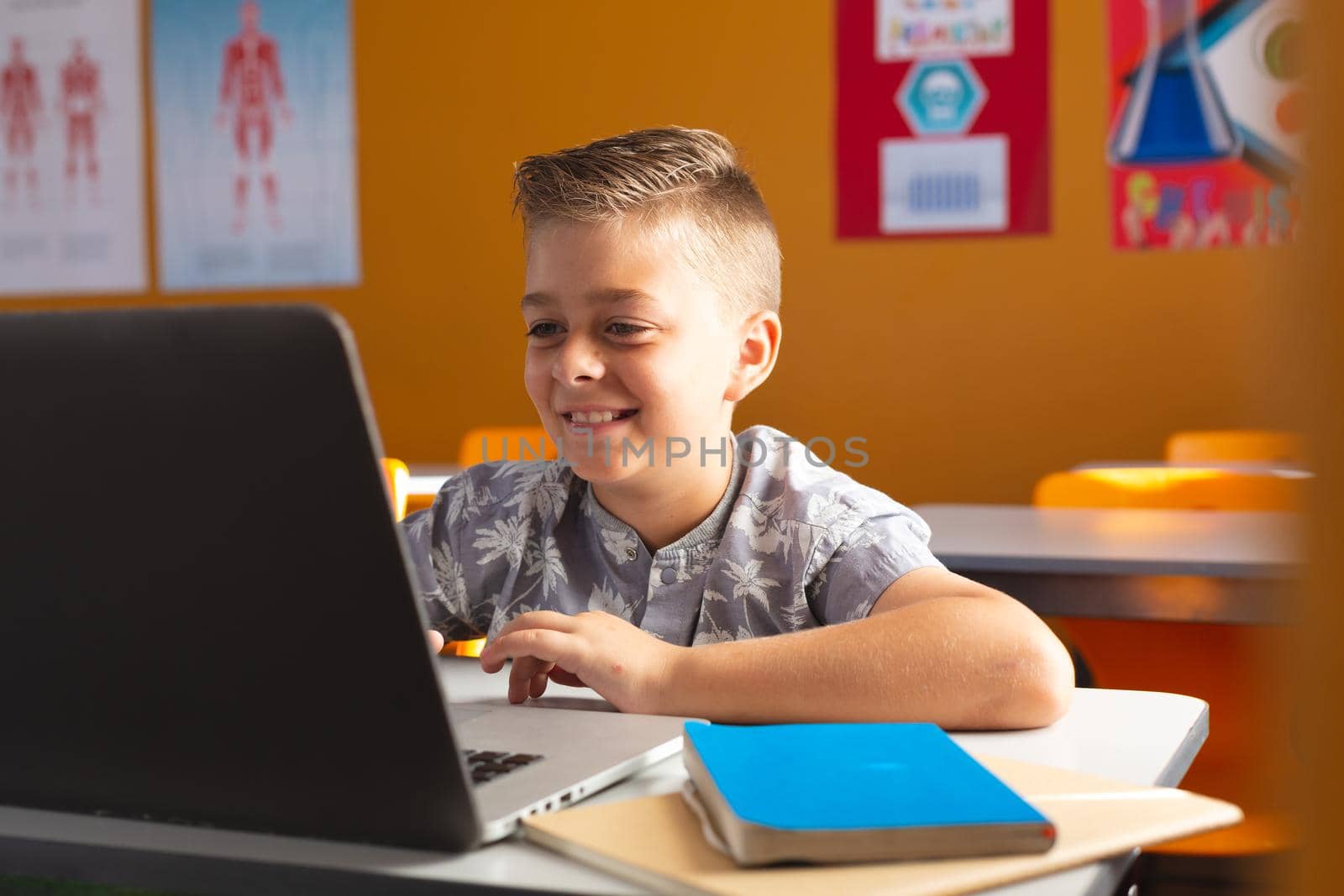 Caucasian boy sitting at a desk in classroom using laptop and smiling. childhood, technology and education at elementary school.