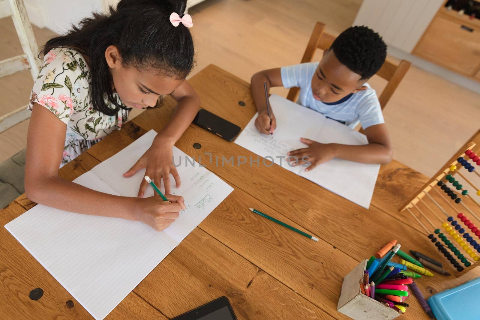 African american boy and girl doing homework at home, sitting at table. family domestic life, spending time working together at home.