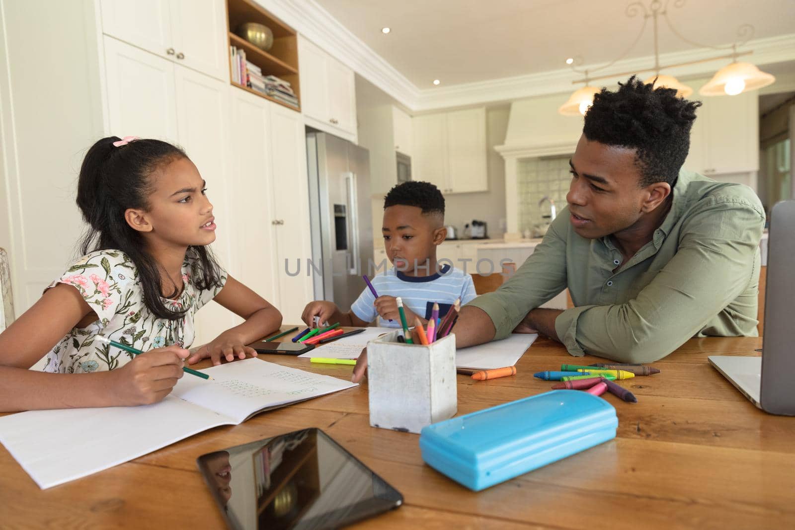 Happy african american father with daughter and son doing homework at home smiling. family domestic life, spending time learning together at home.