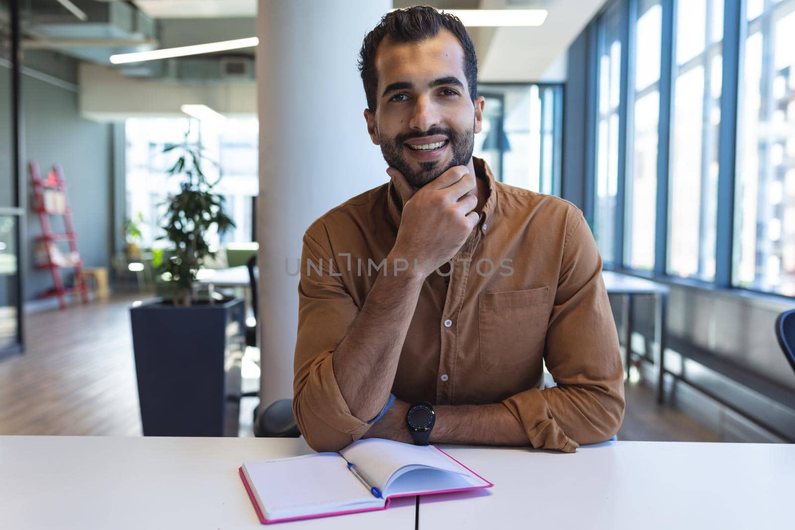 Portrait of mixed race male creative worker sitting at desk looking at camera by Wavebreakmedia