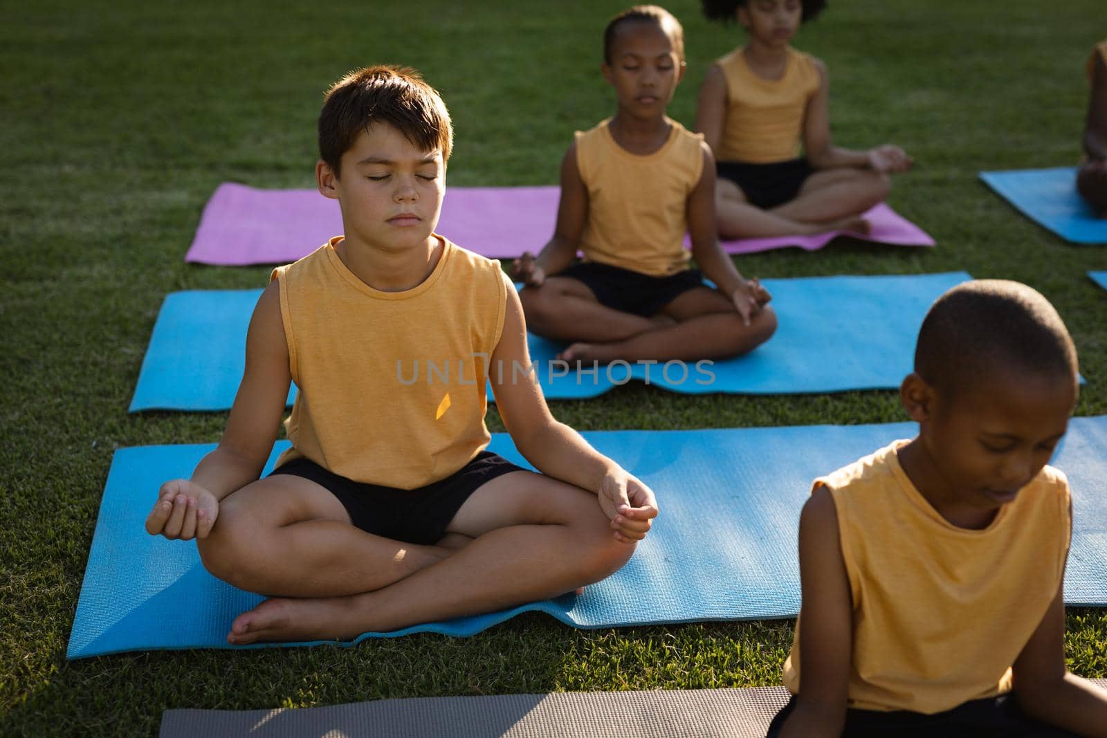 Caucasian boy practicing yoga and meditating sitting on yoga mat in garden at school. school and education concept