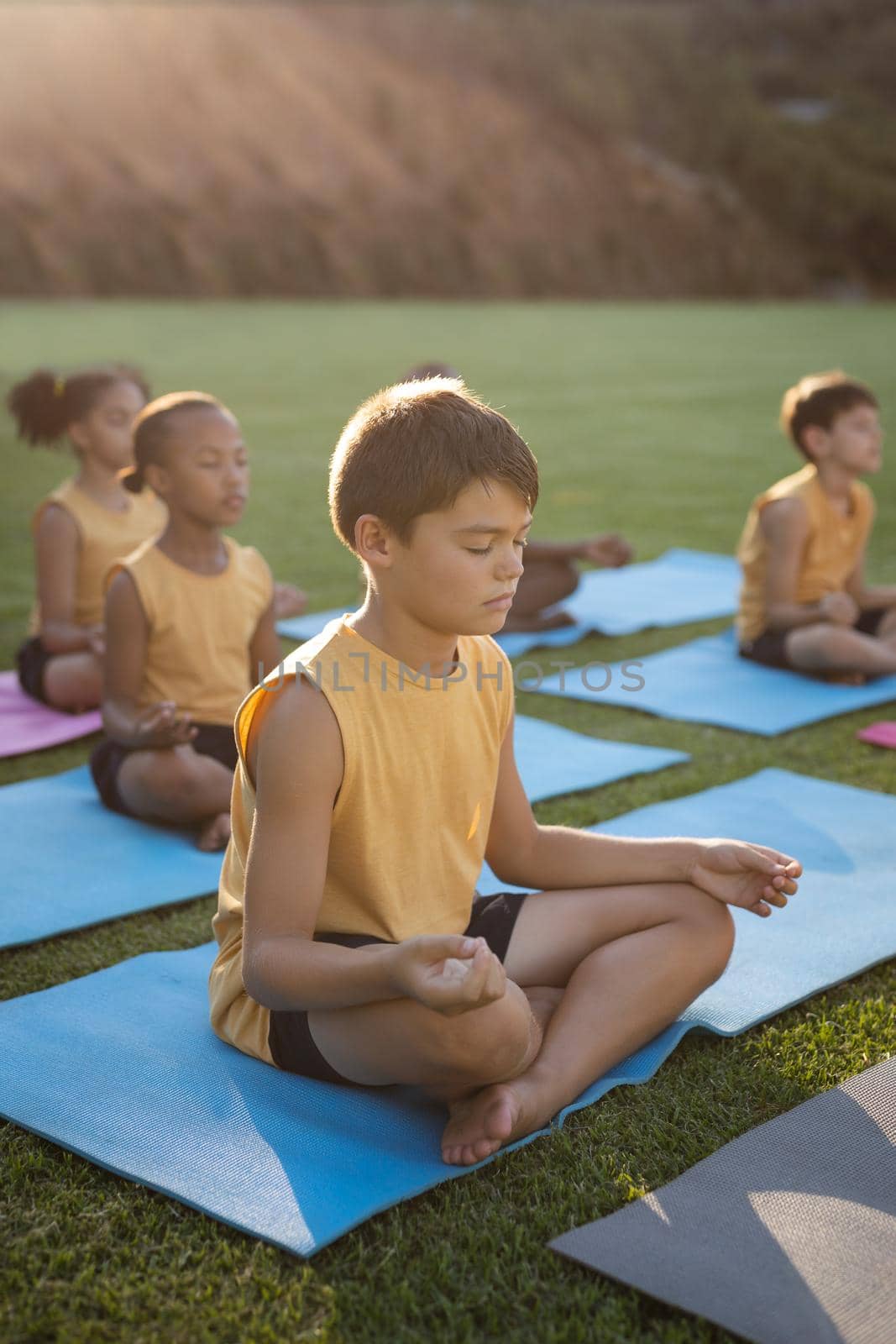 Caucasian boy practicing yoga and meditating sitting on yoga mat in the garden at school by Wavebreakmedia