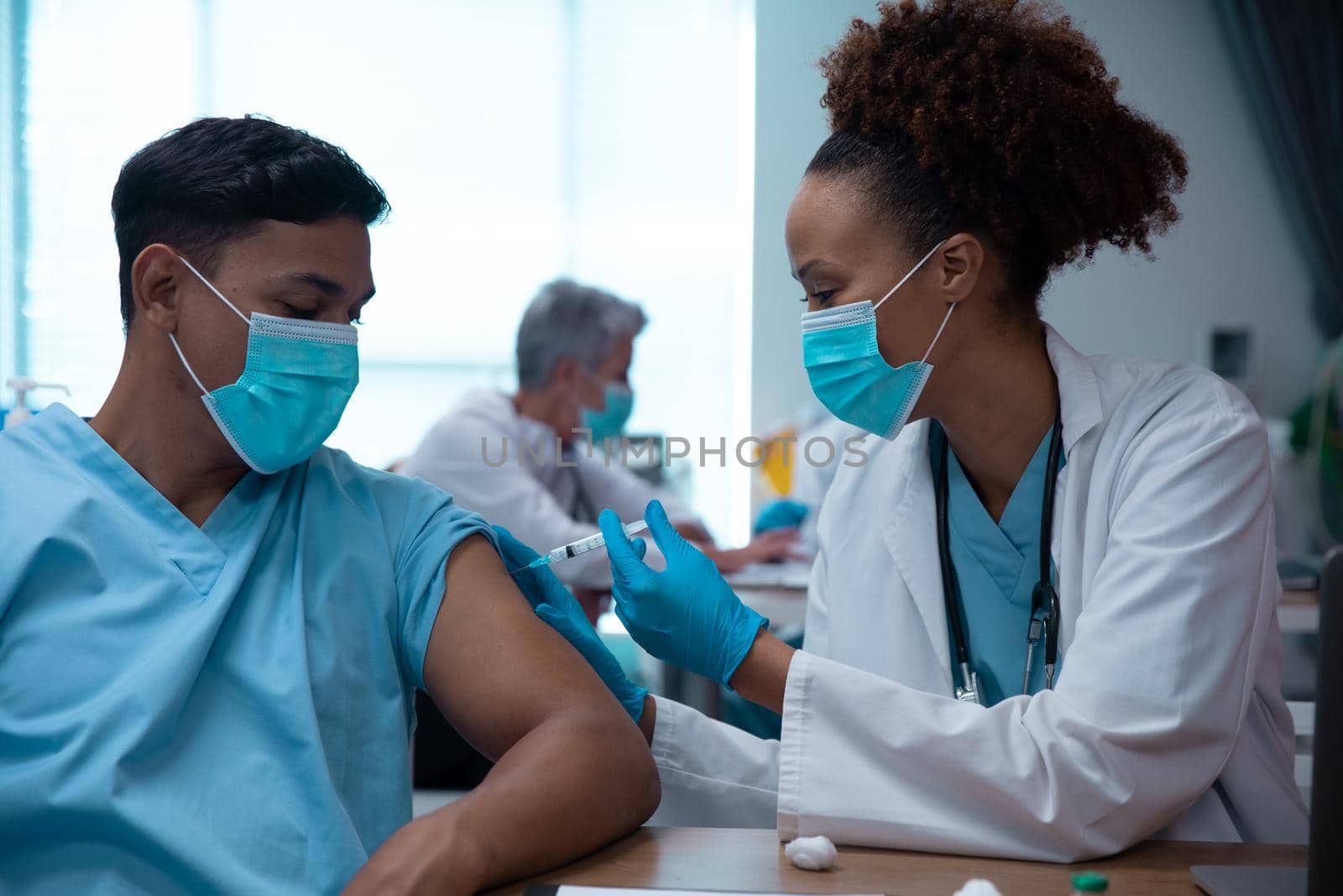 Mixed race couple of doctors wearing face masks making injection. medicine, health and healthcare services during coronavirus covid 19 pandemic.