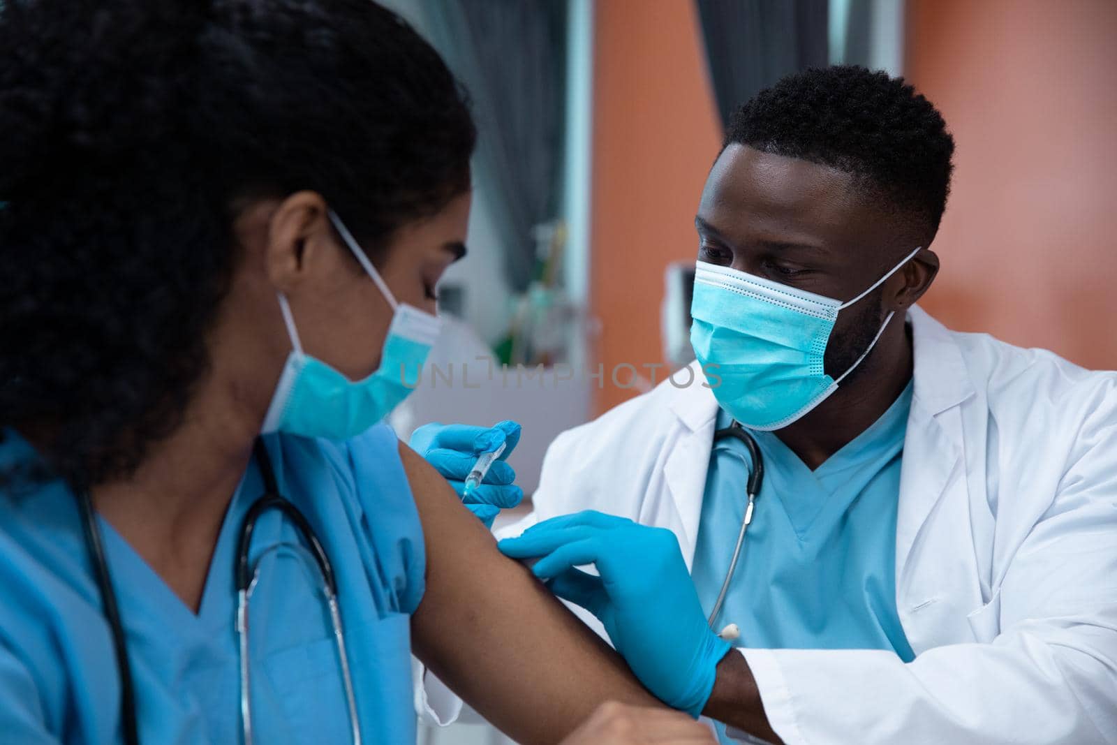 Mixed race couple of doctors wearing face masks making injection. medicine, health and healthcare services during coronavirus covid 19 pandemic.