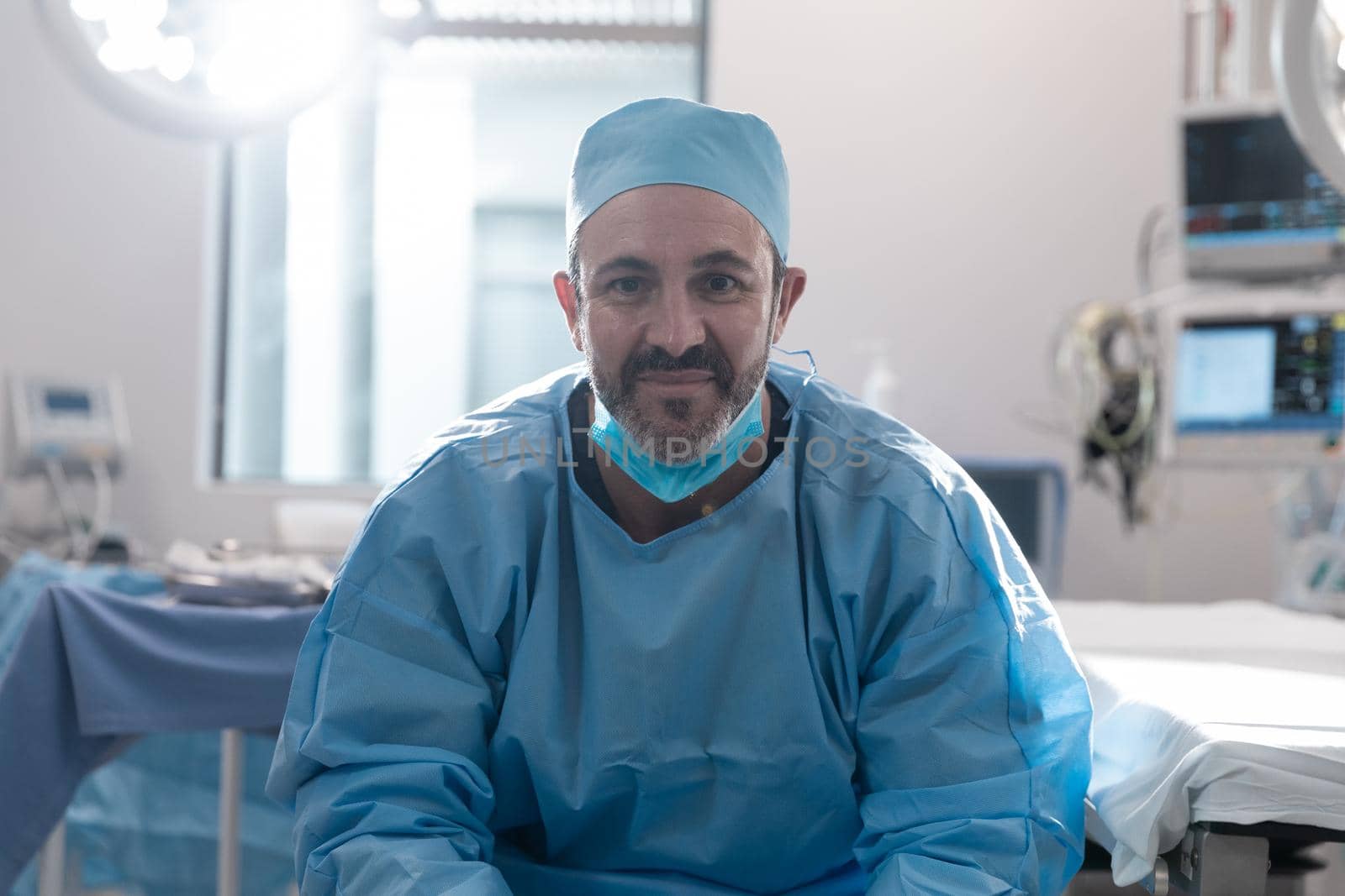 Smiling caucasian male surgeon with face mask wearing protective clothing in operating theatre by Wavebreakmedia