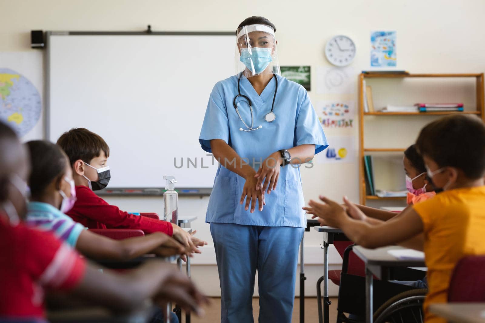 Female health worker showing students to use hands sanitizer at elementary school. education back to school health safety during covid19 coronavirus pandemic.