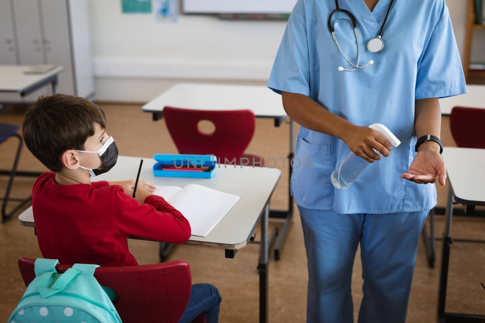 Mid section of female health worker showing students to use hands sanitizer at elementary school by Wavebreakmedia