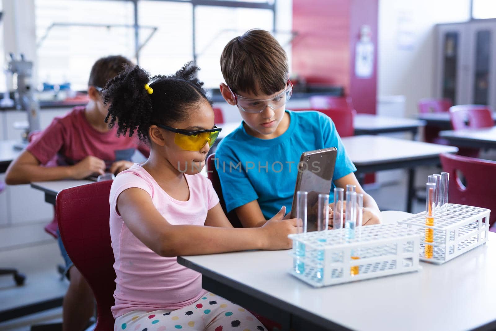 African american girl and caucasian boy using digital tablet in science class at elementary school. school and education concept