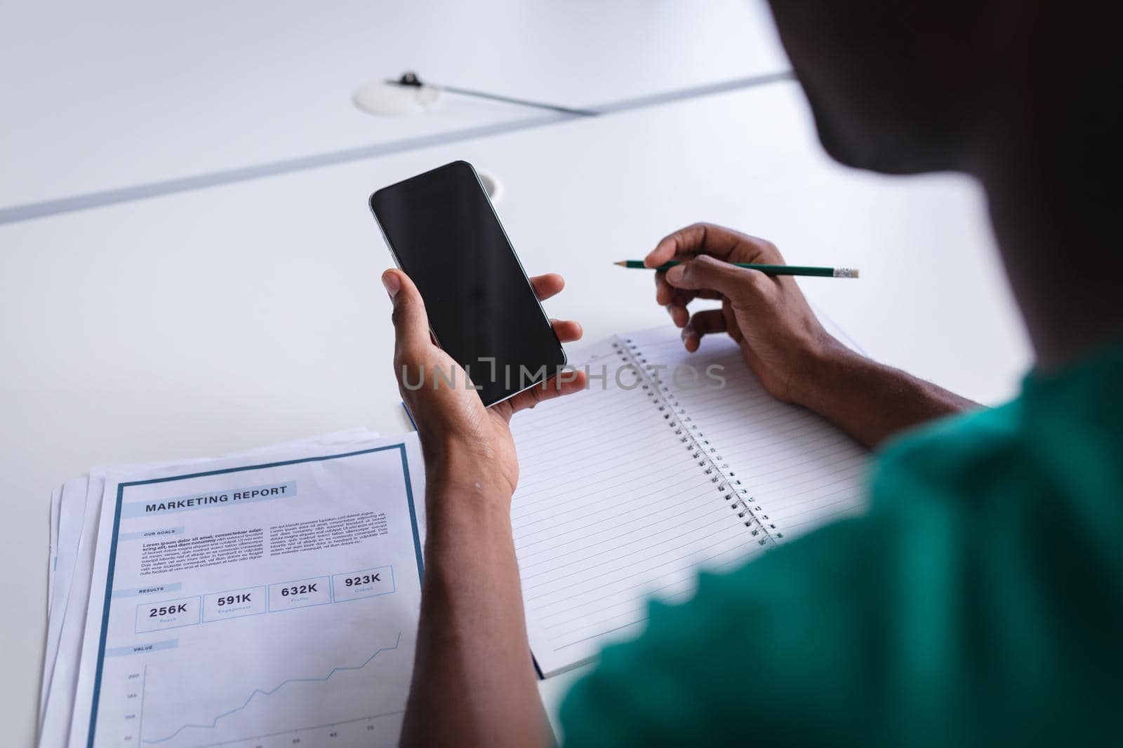 African american businessman sitting in office having video call using smartphone and making notes by Wavebreakmedia