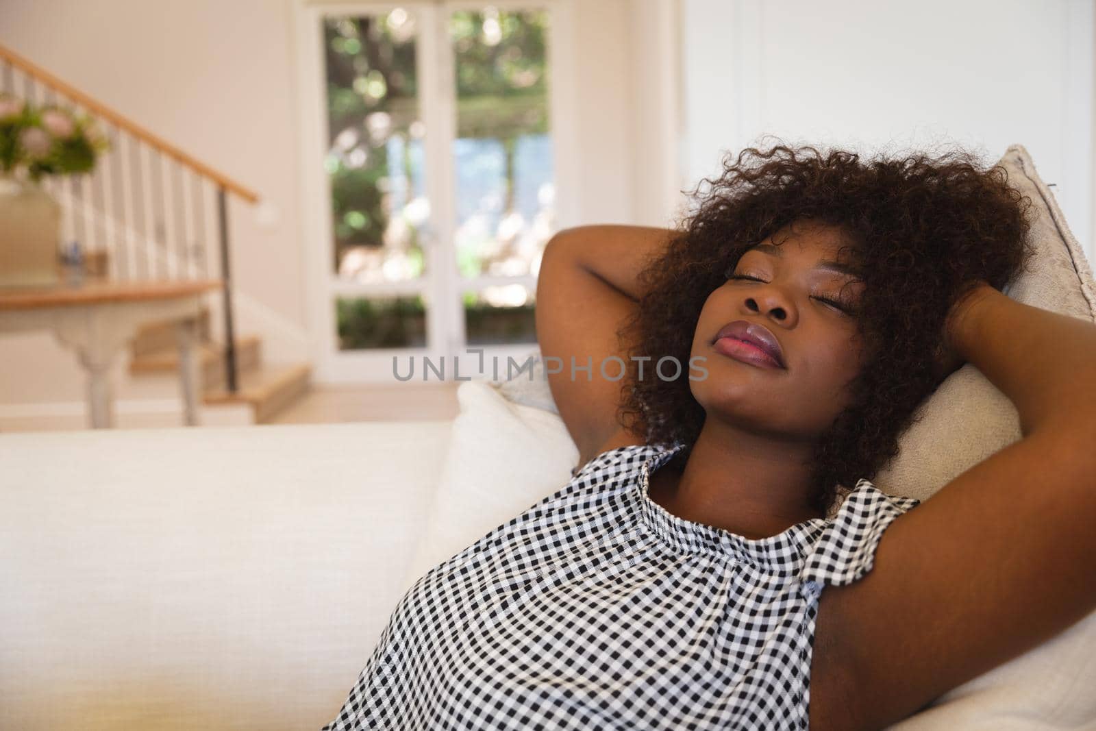 Portrait of african american woman with eyes closed reclining on sofa at home. domestic lifestyle, enjoying leisure time at home.