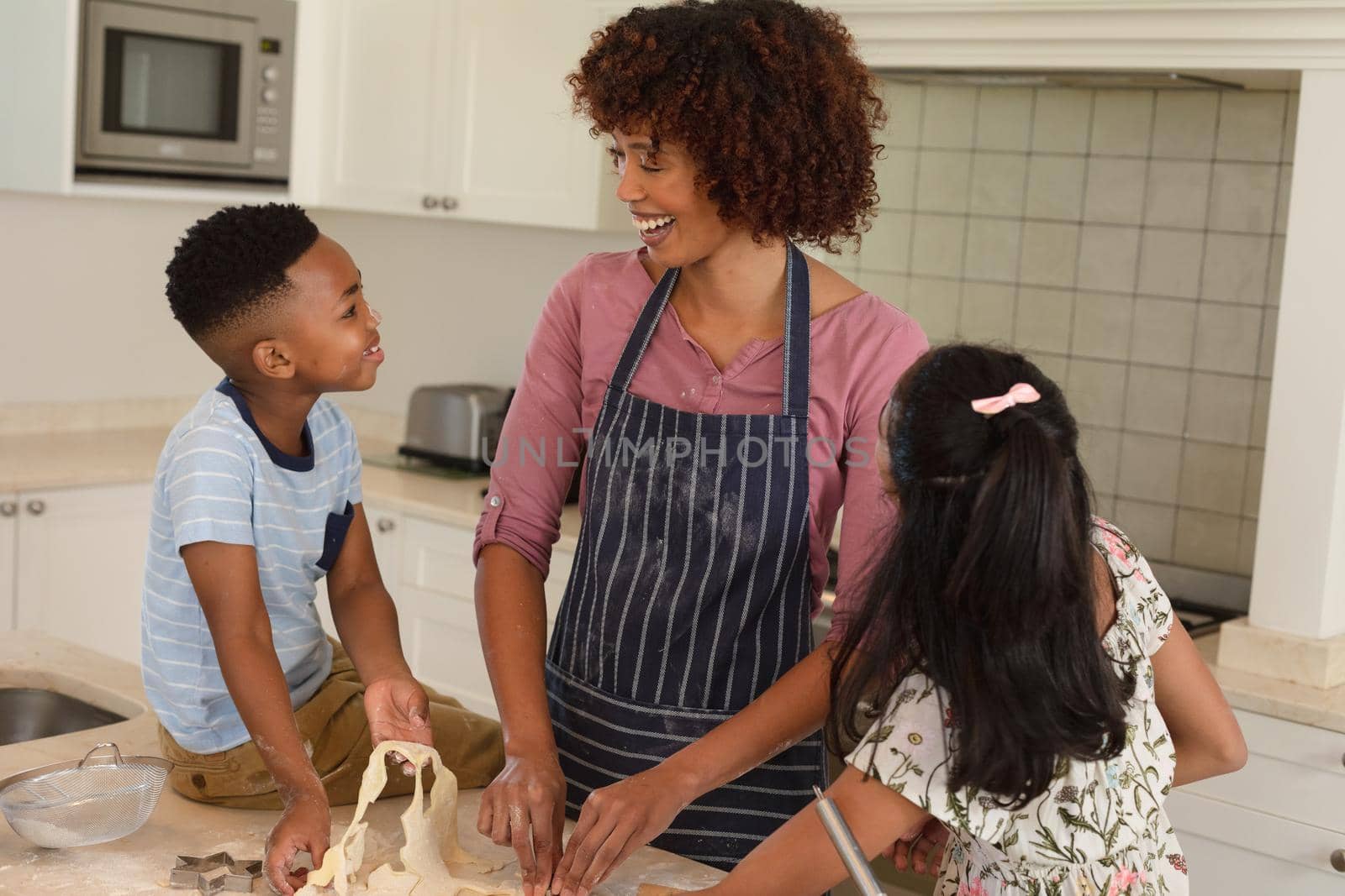 Happy african american mother with son and daughter baking in kitchen, cutting cookies. family enjoying quality free time together.