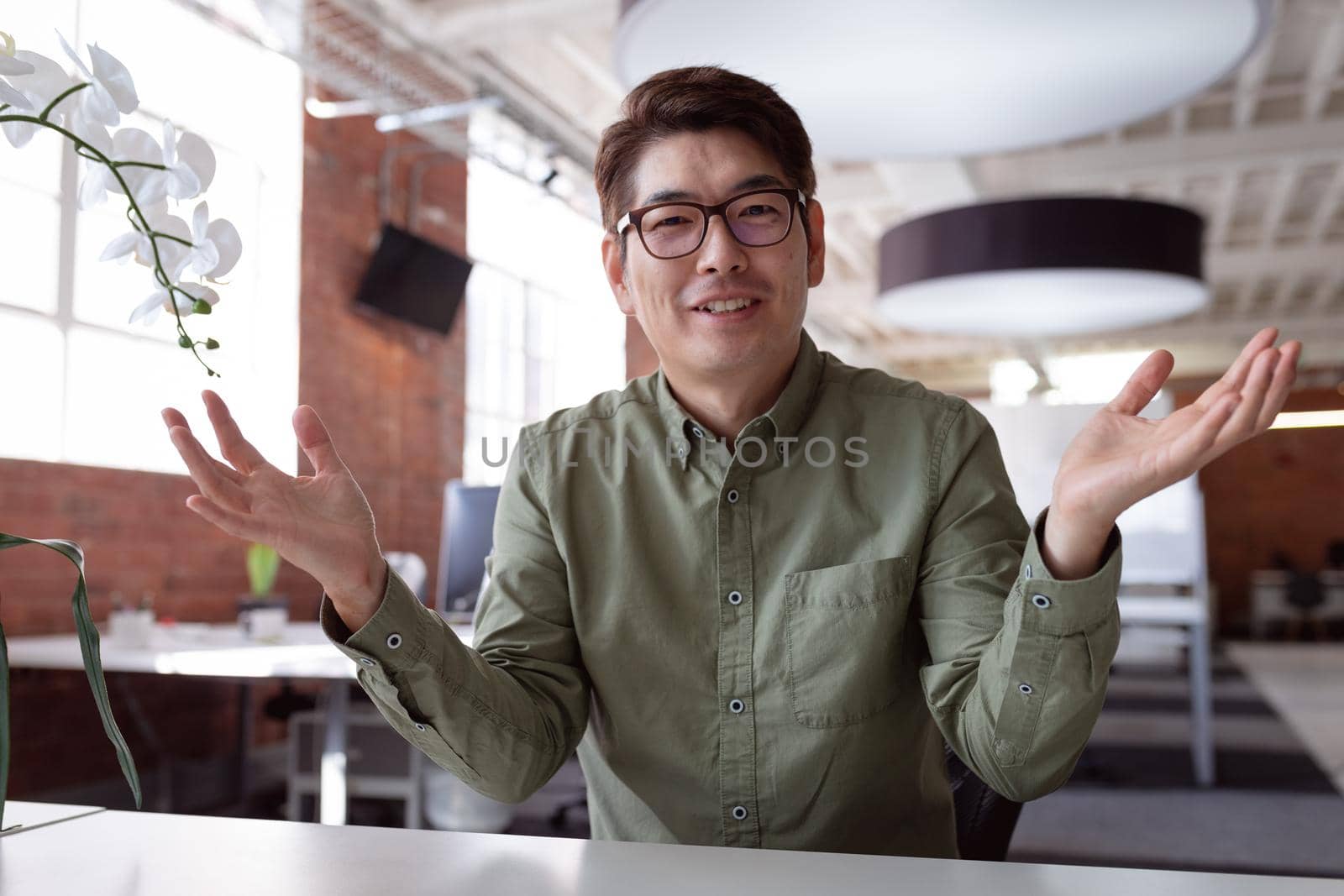 Happy asian businessman sitting at desk talking and gesturing during video call by Wavebreakmedia