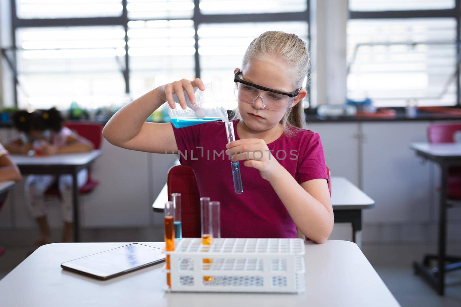 Caucasian girl pouring chemical from beaker into test tube in science class at laboratory. school and education concept