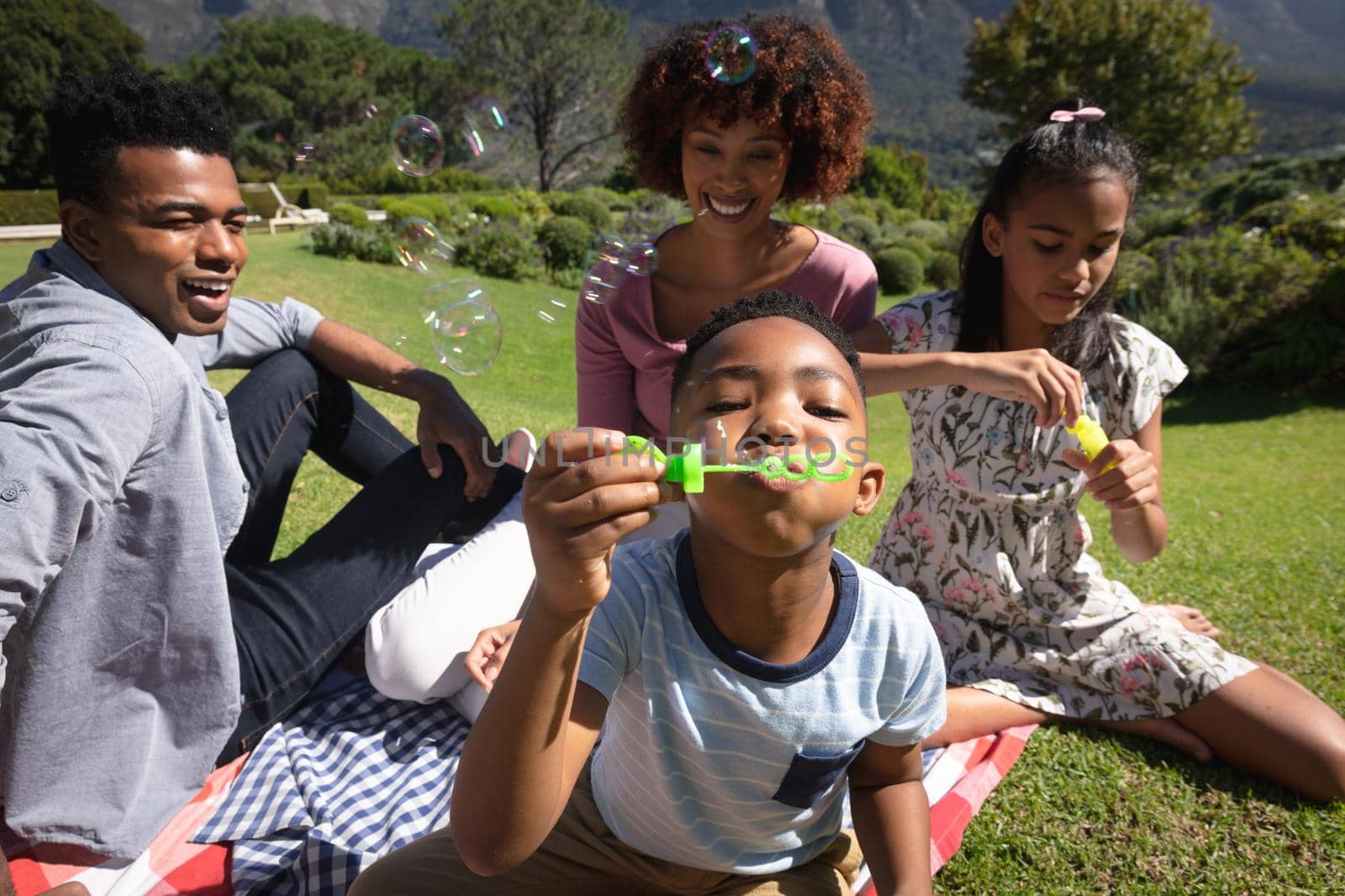 Happy african american couple with son and daughter outdoors, blowing bubbles in sunny garden by Wavebreakmedia