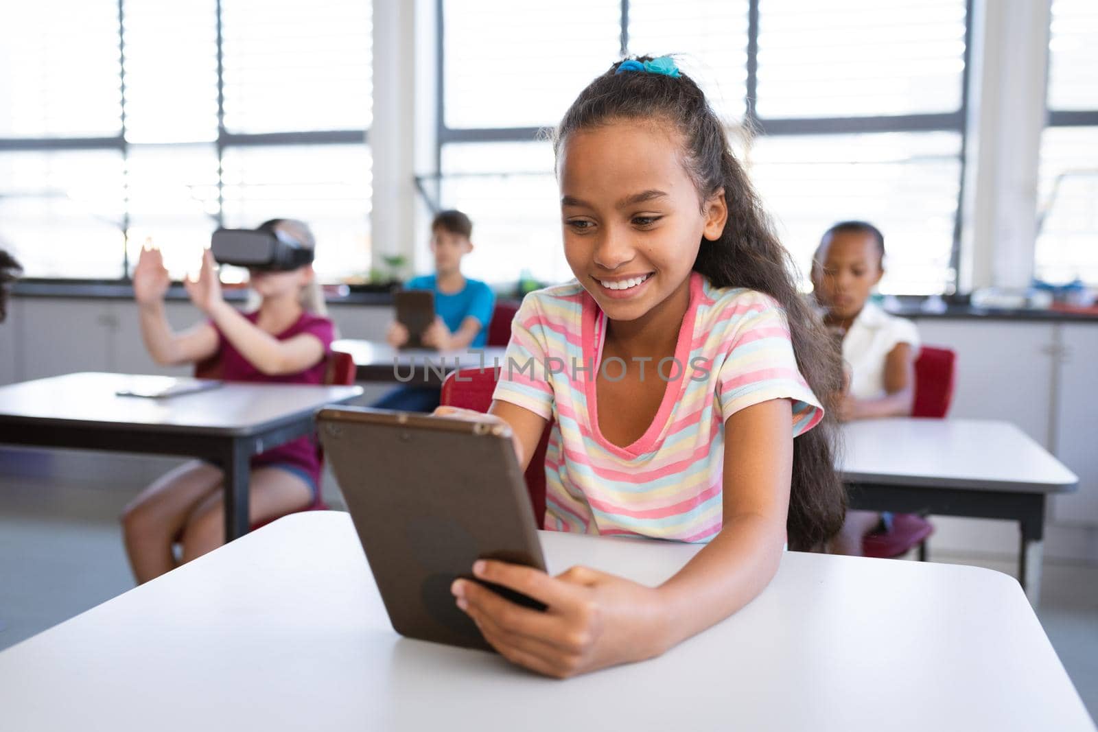 Smiling african american girl using digital tablet while sitting on her desk in class at school. school and education concept