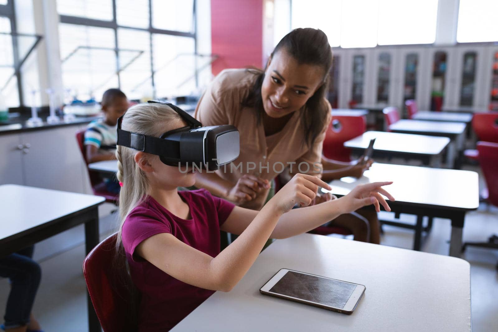 African american female teacher teaching caucasian girl to use vr headset in the class at school by Wavebreakmedia