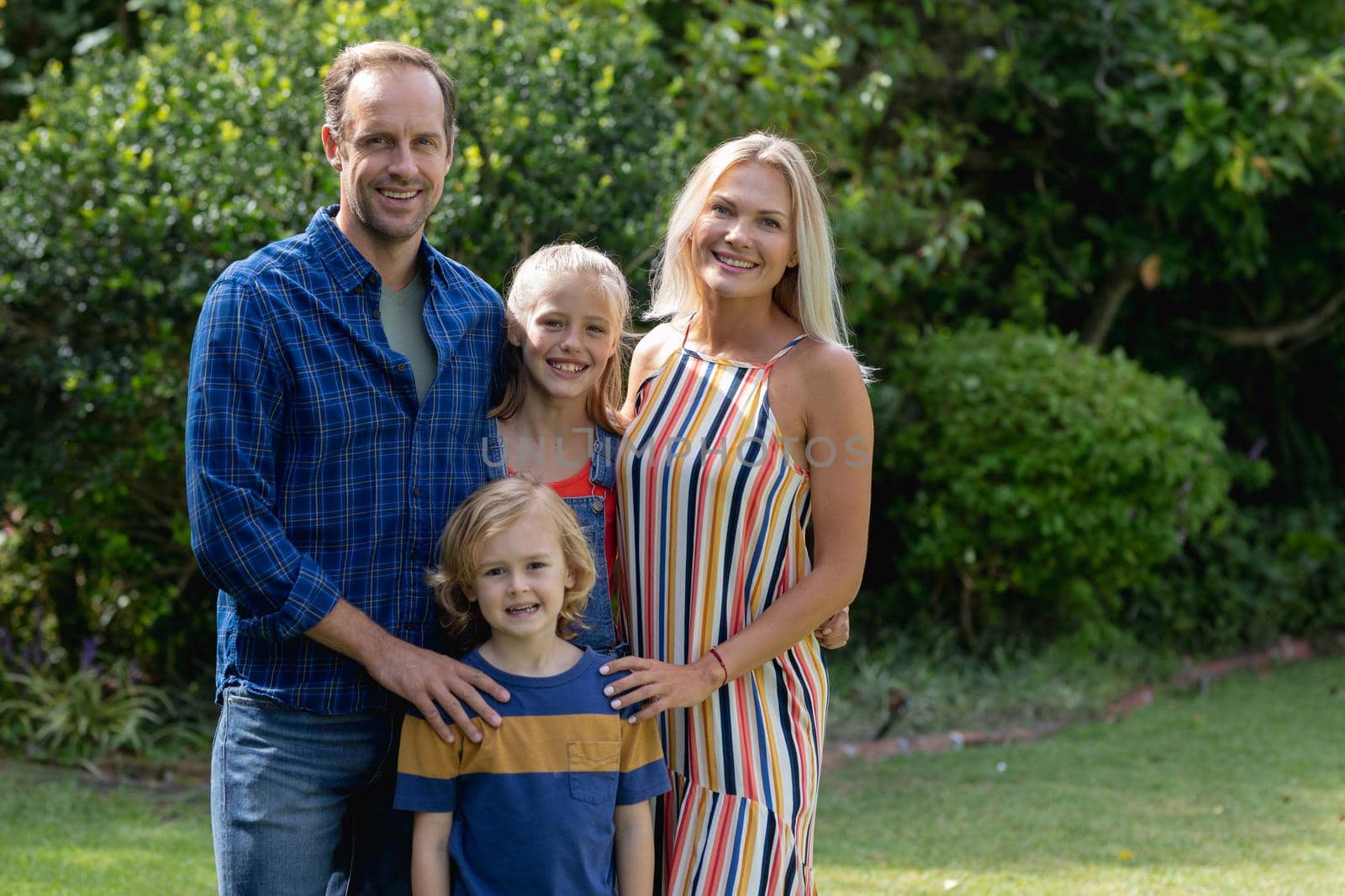 Portrait of caucasian parents with son and daughter standing in garden smiling and embracing. staying at home in isolation during quarantine lockdown.