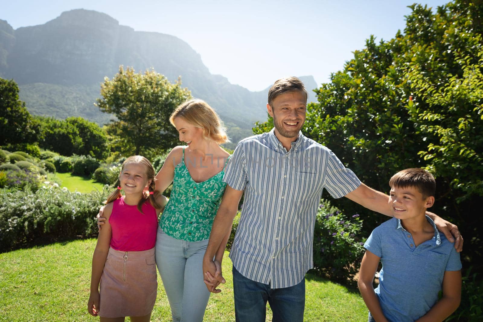 Happy caucasian couple with daughter and son outdoors, walking in sunny garden. family enjoying quality free time together.