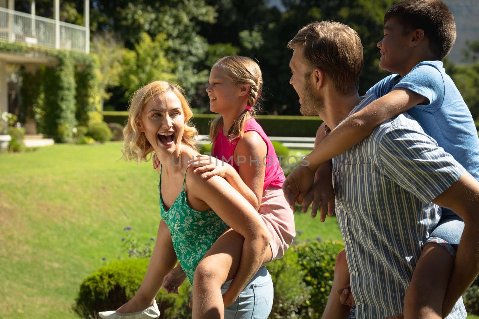 Happy caucasian couple with daughter and son outdoors, playing in sunny garden. family enjoying quality free time together.