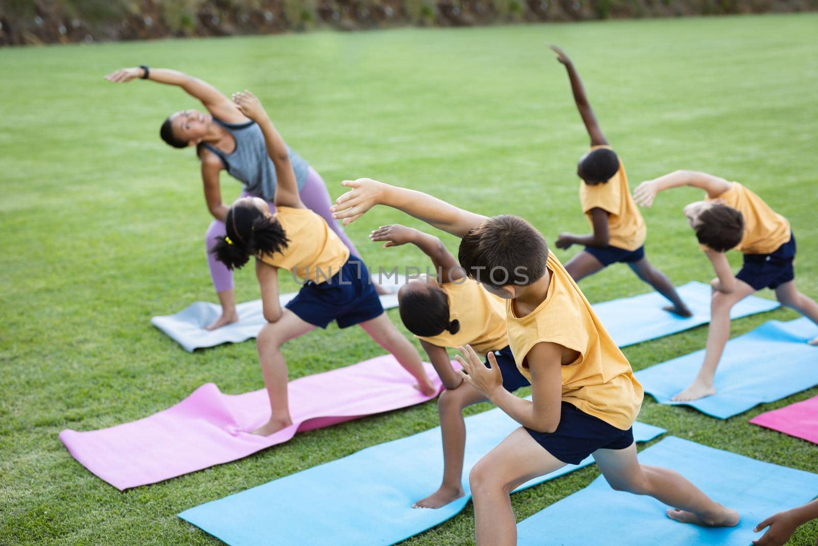 Female teacher and group of diverse students performing stretching exercise in the garden at school. school and education concept