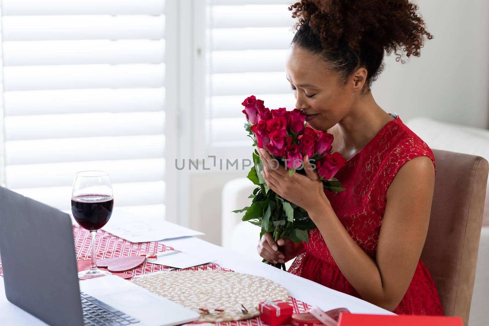 African american woman smelling flower bouquet on videocall at home by Wavebreakmedia