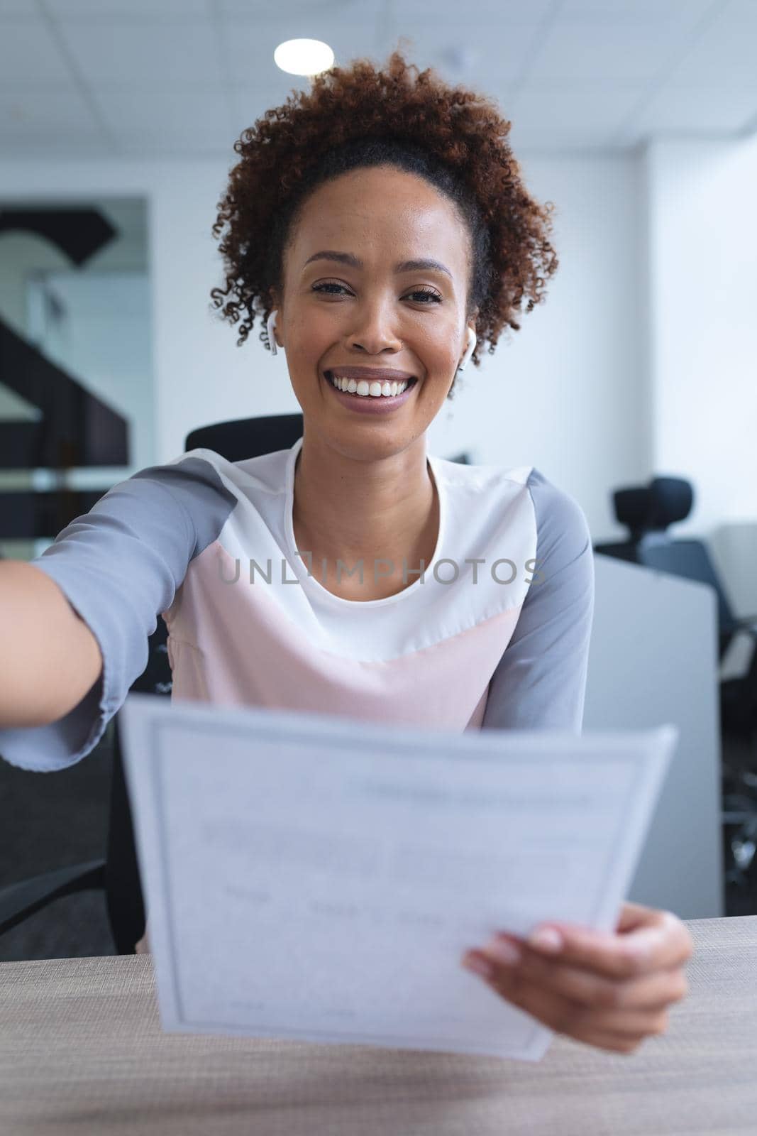 Portrait of mixed race businesswoman sitting at desk smiling, having video call. online meeting, working in isolation during quarantine lockdown.