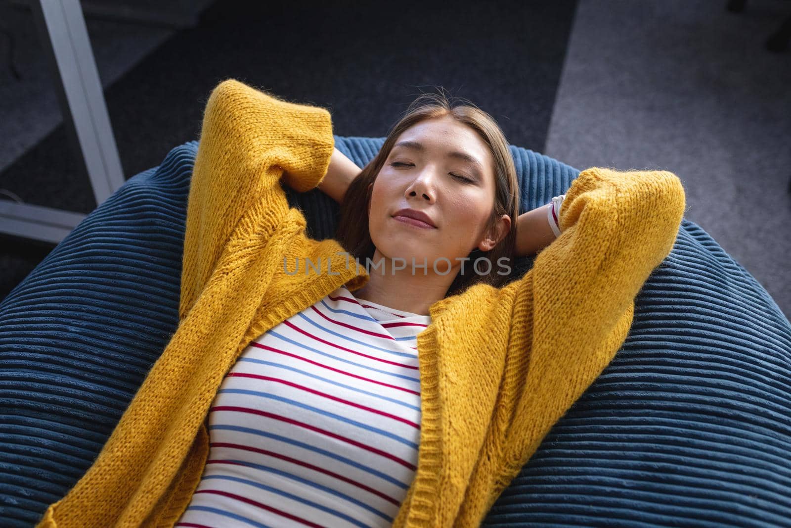 Mixed race businesswoman chilling in office relaxing space lying in beanbag by Wavebreakmedia