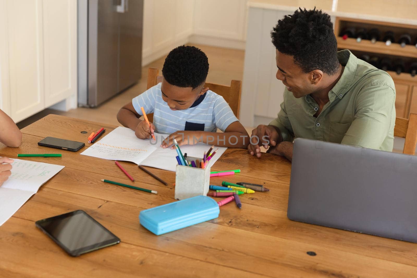 Happy african american father with daughter and son doing homework at home smiling by Wavebreakmedia