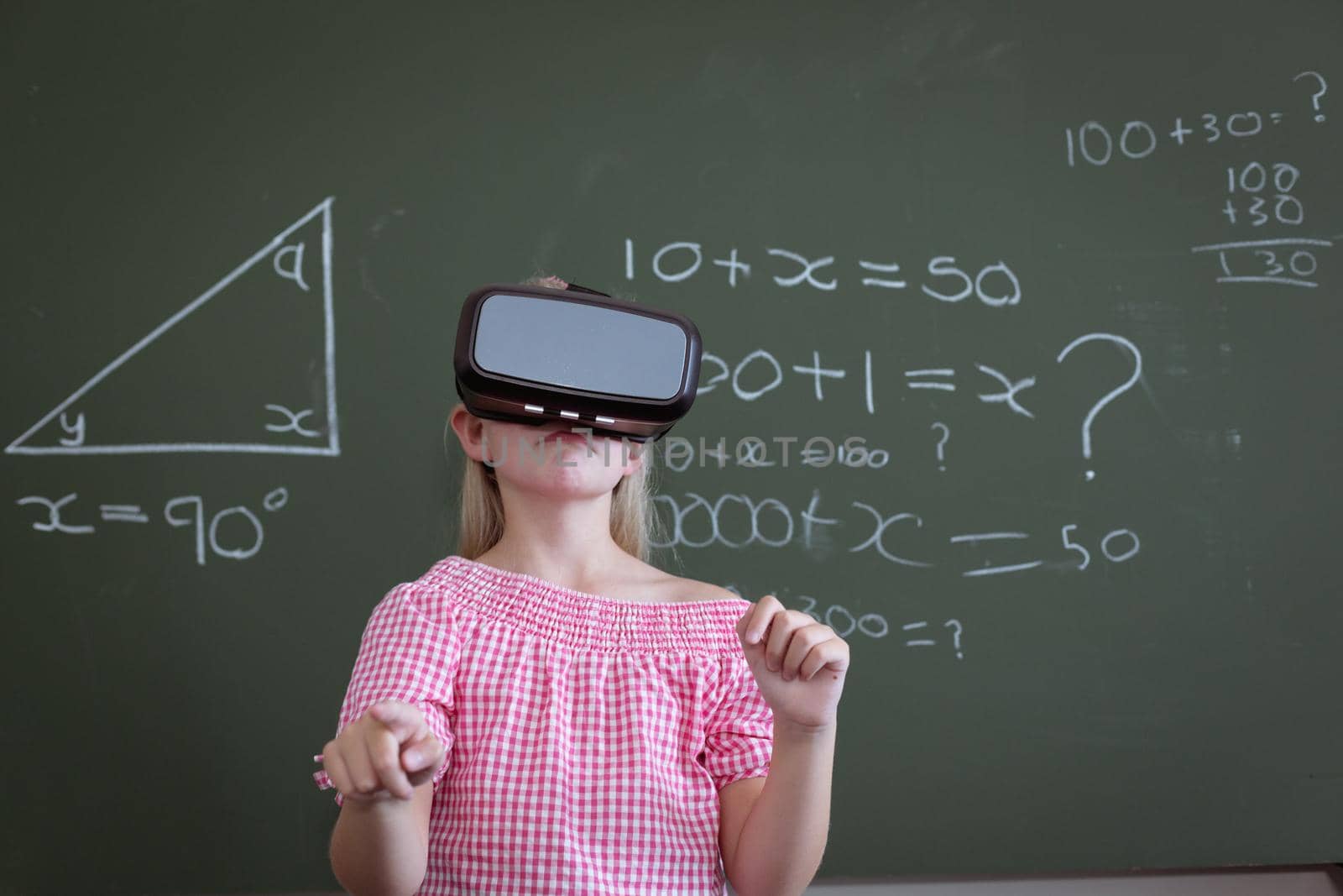 Caucasian schoolgirl standing at chalkboard in classroom wearing vr headset by Wavebreakmedia