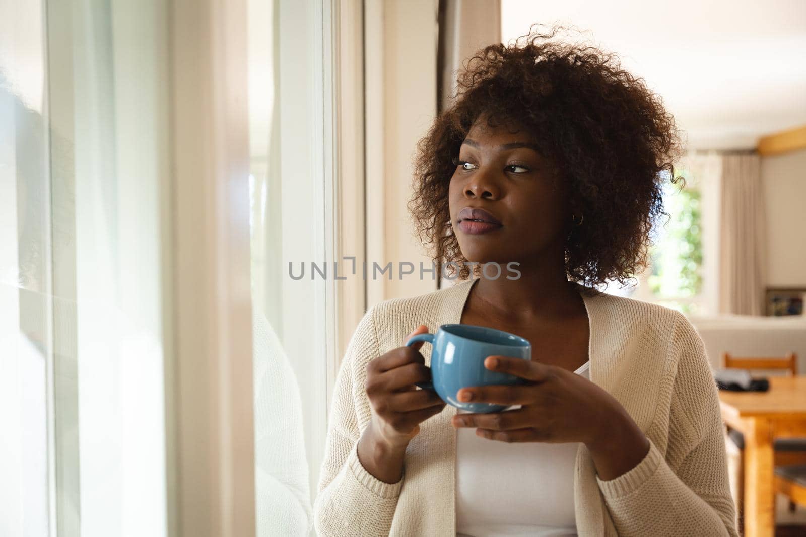 Thoughtful african american woman standing in dining room holding cup of coffee. spending free time at home.