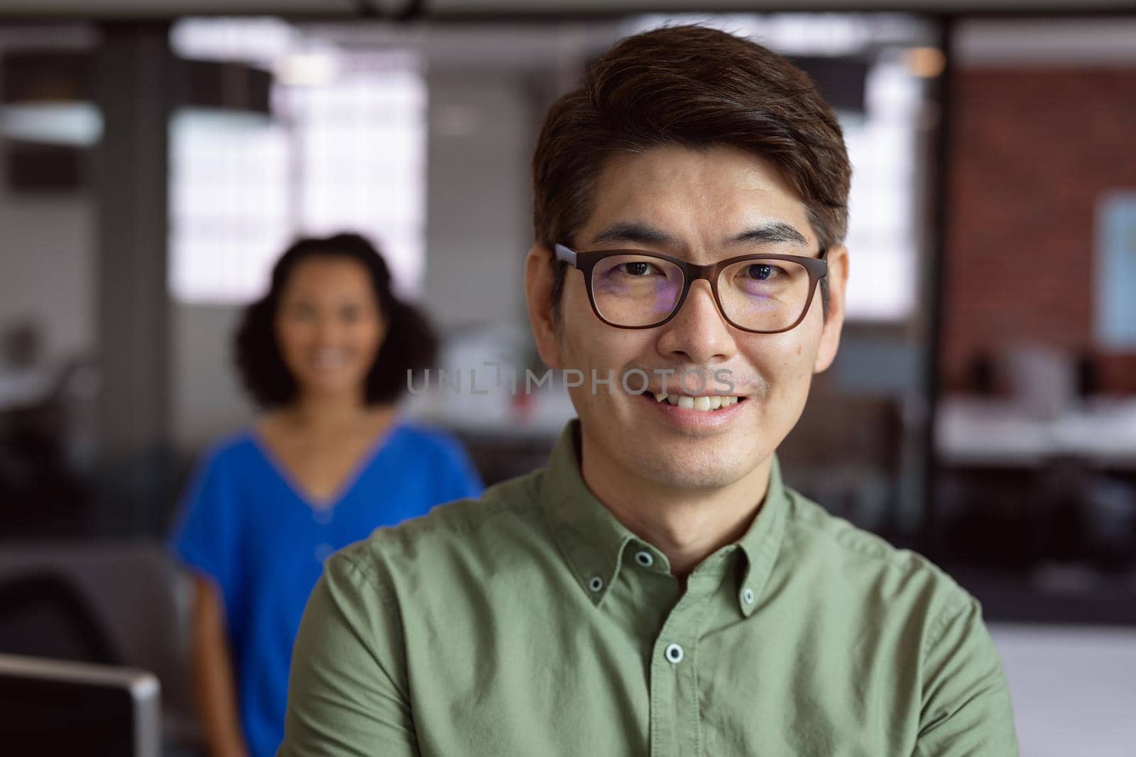 Portrait of smiling asian businessman standing in office with female colleague in background. working in business at a modern office.