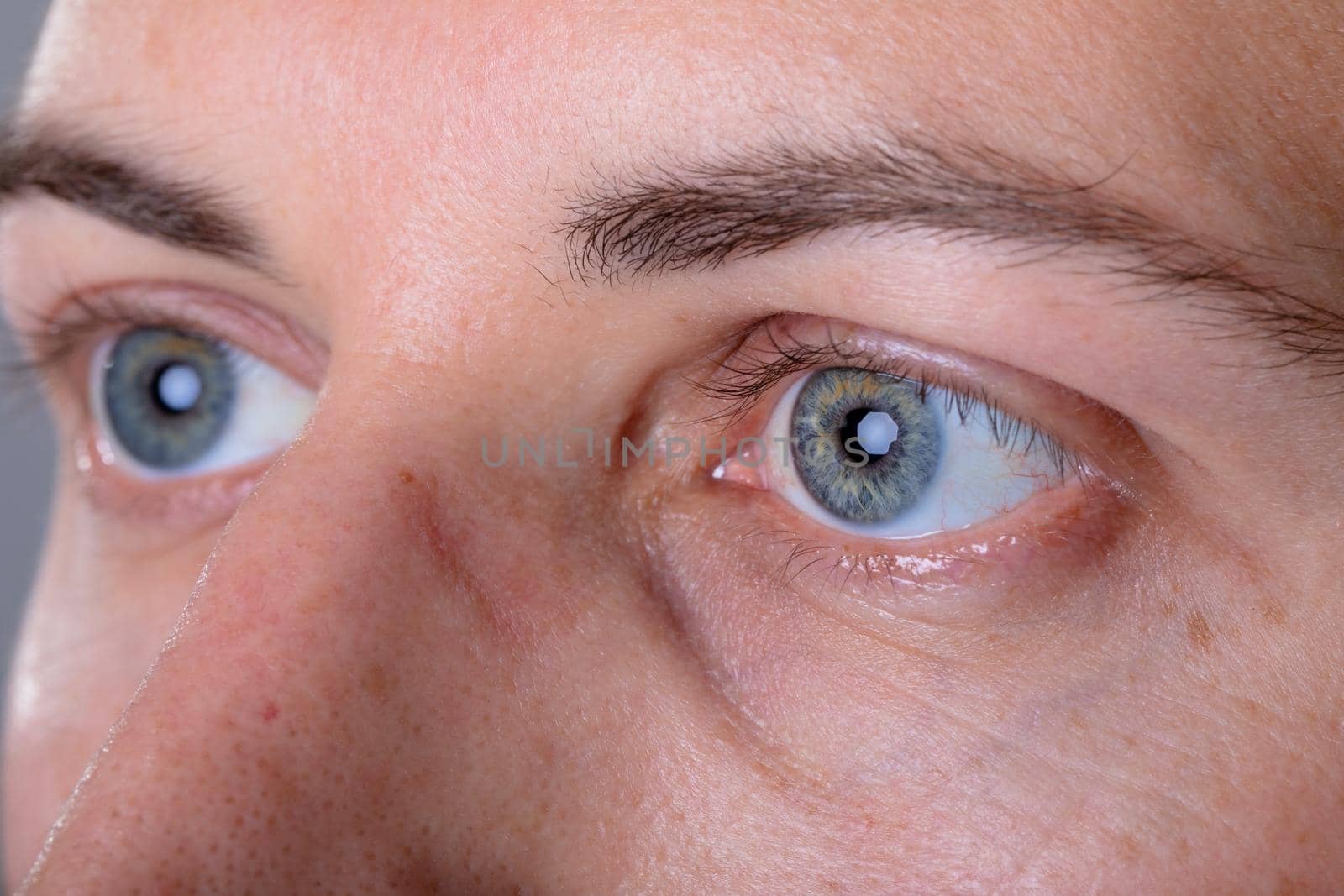 Close up of blue eyes of caucasian businessman, isolated on grey background by Wavebreakmedia