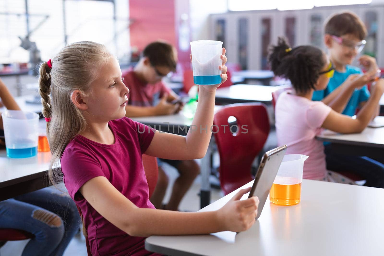 Caucasian boy holding a beaker and digital tablet in science class at laboratory. school and education concept