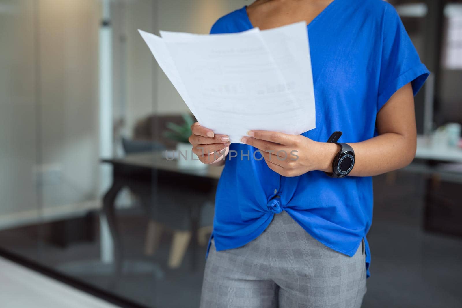 Midsection of african american businesswoman looking at paperwork standing in office by Wavebreakmedia