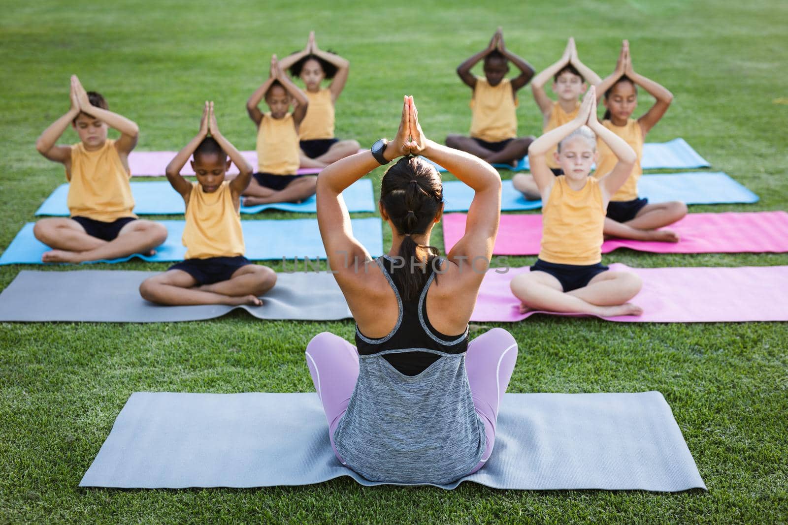 Female teacher and group of diverse students practicing yoga and meditating in the garden at school. school and education concept