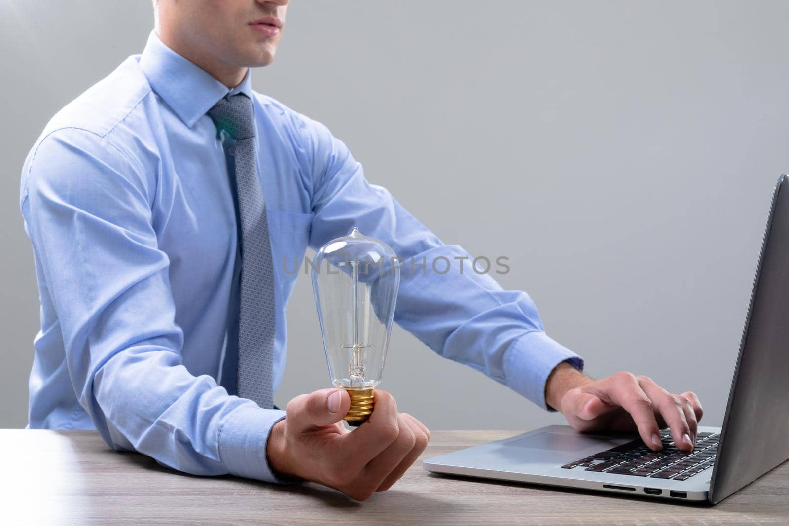 Caucasian businessman holding light bulb using laptop, isolated on grey background. business technology, communication and growth concept.